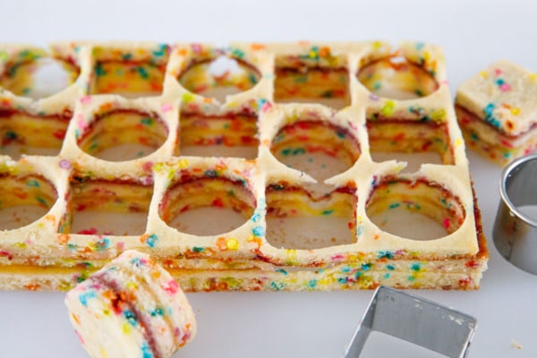 Cutting out shapes of layered funfetti cake to make petit fours.