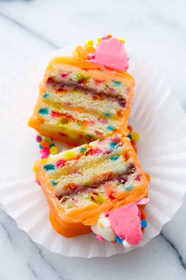 Orange-glazed "Funfetti Fours" cut in half to show the layers of funfetti cake, apricot and raspberry jams.