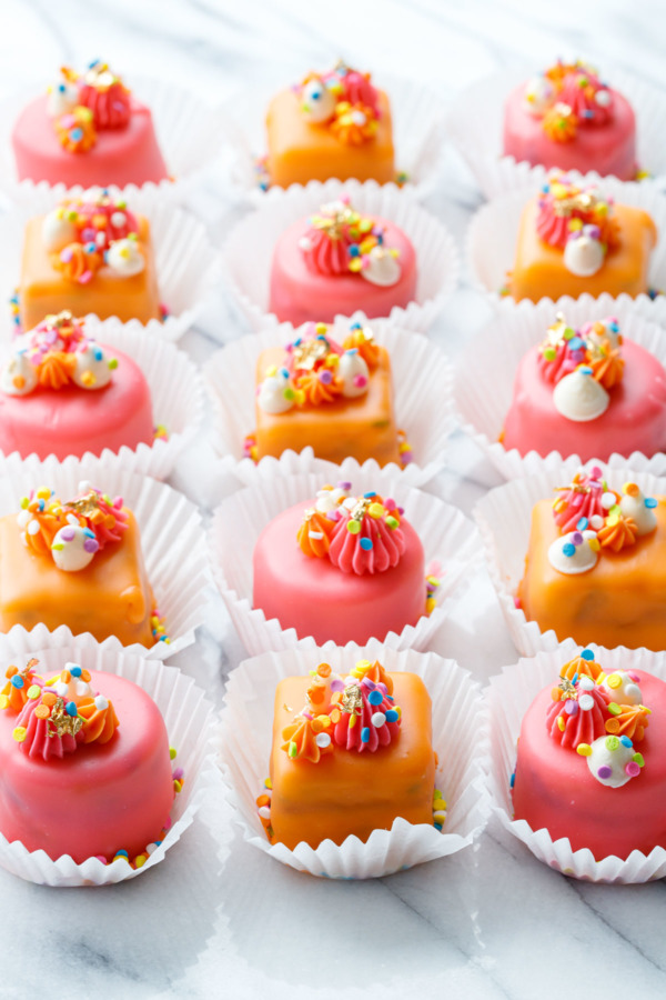 Rows of pink and orange "Funfetti Fours" with buttercream decorations and rainbow sprinkles