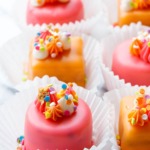 Rows of pink and orange "Funfetti Fours" with buttercream decorations and rainbow sprinkles