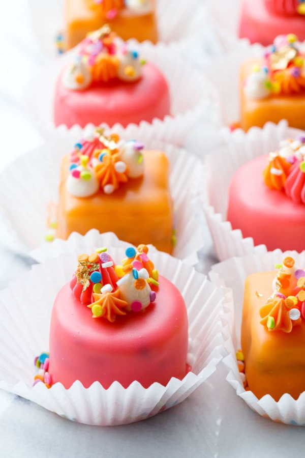 Rows of pink and orange "Funfetti Fours" with buttercream decorations and rainbow sprinkles