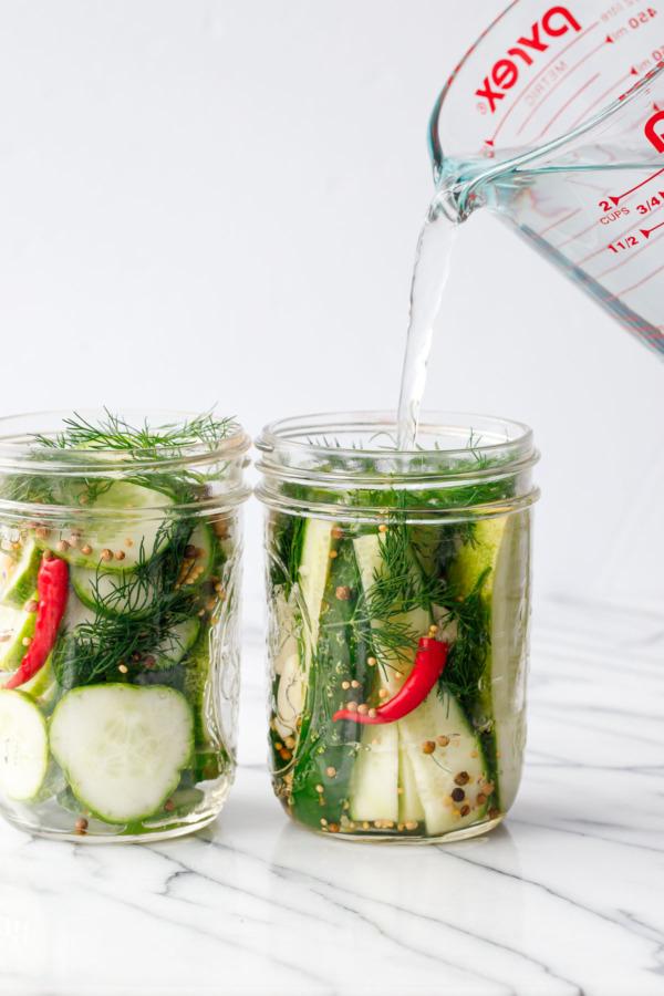 Pouring the vinegar brine into pint mason jars to make refrigerator pickles