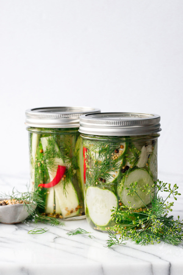 Two jars of pickles ready to go in the refrigerator, one cut into spears and one cut into chips.