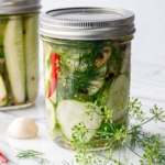 Two jars of spicy garlic dill refrigerator pickles, with fresh dill and dill flowers