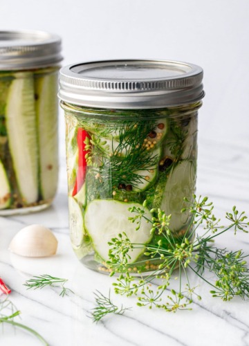 Two jars of spicy garlic dill refrigerator pickles, with fresh dill and dill flowers