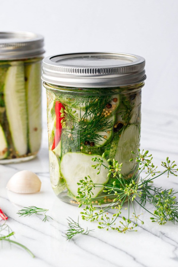 Two jars of spicy garlic dill refrigerator pickles, with fresh dill and dill flowers
