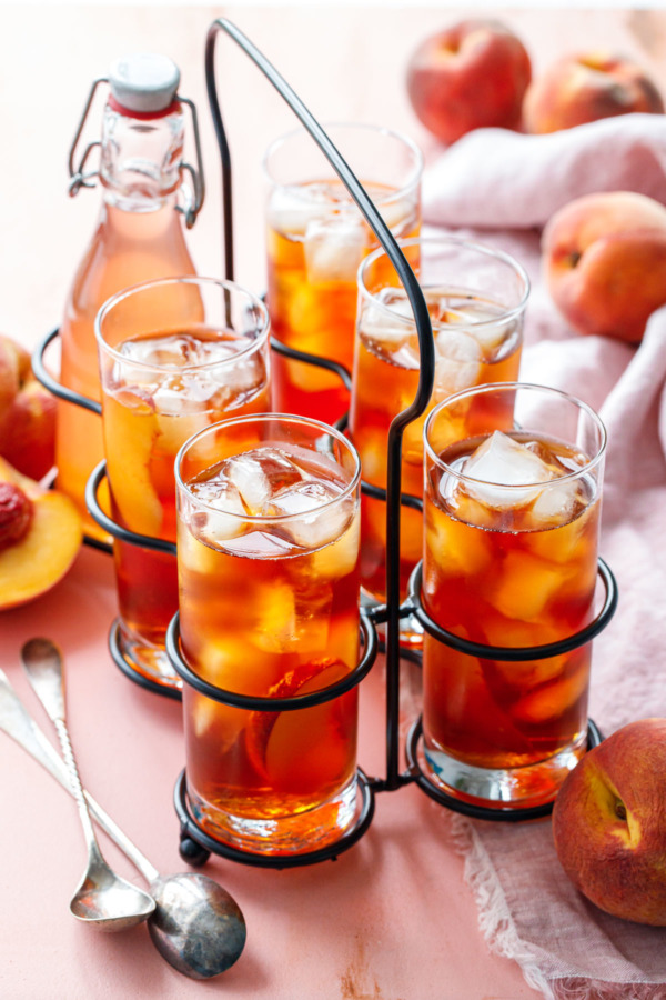 A vintage drink caddy with 5 glasses of Cold Brew Peach Iced Tea, and one bottle of peach sugar syrup