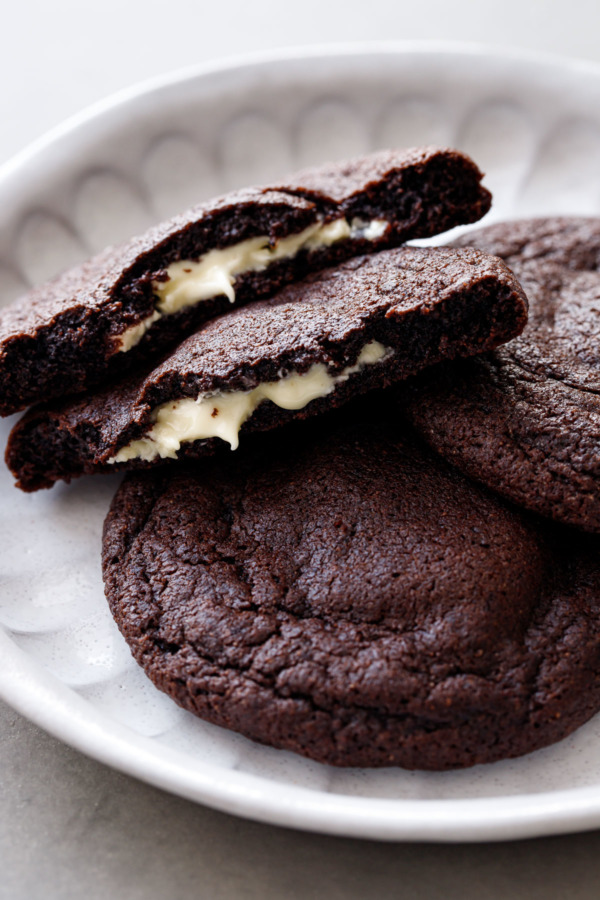 Close up of White Chocolate-Stuffed Chocolate Cookies, one cookie broken in half showing melted white chocolate center.