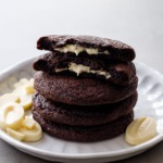 Stack of White Chocolate-Stuffed Chocolate Cookies, top cookie broken in half to show the melted white chocolate center.