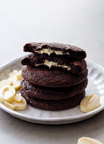 Stack of White Chocolate-Stuffed Chocolate Cookies, top cookie broken in half to show the melted white chocolate center.