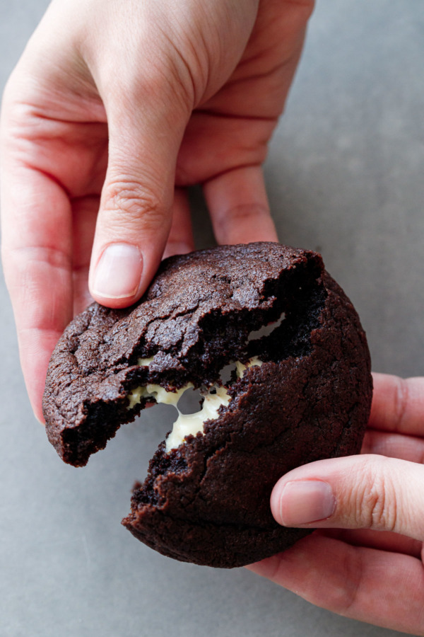 Hands breaking a chocolate cookie in half to reveal the molten white chocolate center.
