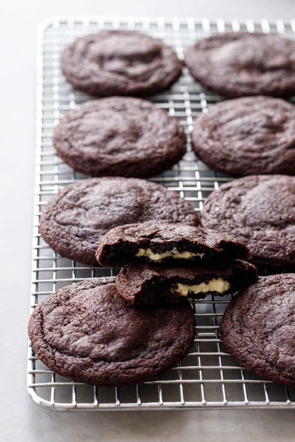 Wire rack with chocolate cookies, one cookie broken in half to show the white chocolate stuffed center.