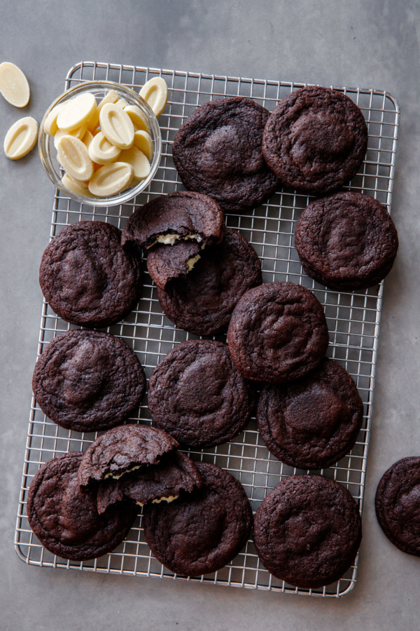 Flat lay view of chocolate cookies arranged randomly on a wire rack, with a bowl of white chocolate pieces.