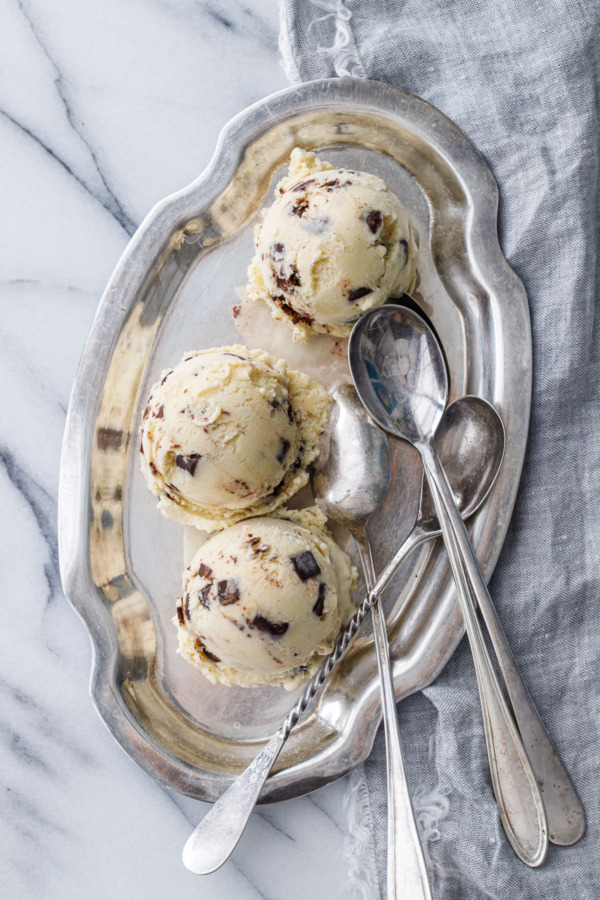 Overhead shot of three scoops of Banana Fudge Chunk Ice Cream on a pewter platter with three spoons on the side.