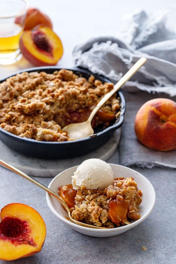 Skillet Bourbon Peach Crisp with fresh peaches on the side and a shot glass of bourbon.