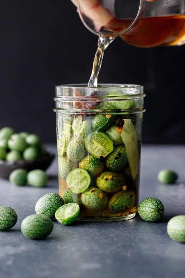 Pouring the cider vinegar-based brine into a jar packed with cucamelons.