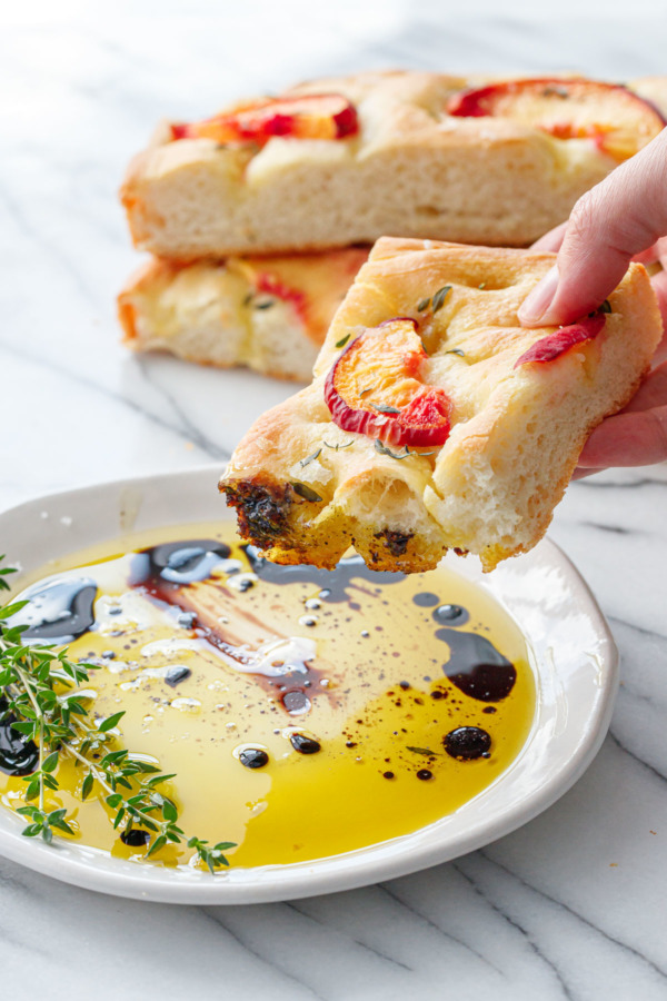 Peach & Fresh Herb Focaccia Bread being dipped into a dish of olive oil and balsamic.