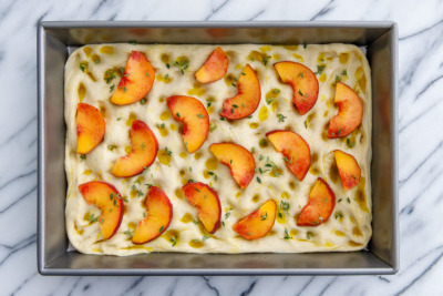 How to make homemade focaccia bread: top with a generous drizzle of olive oil, sliced peaches, fresh herbs and coarse sea salt.