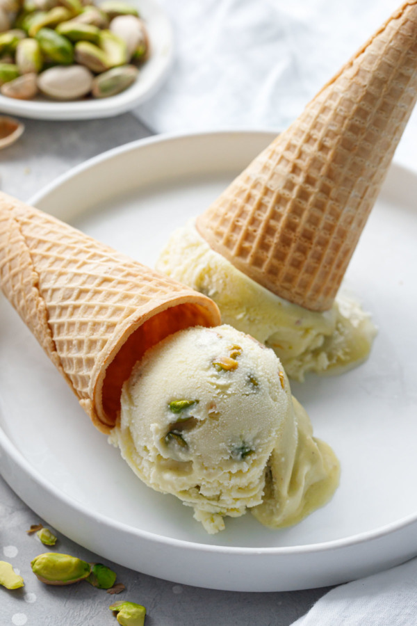 Two cones of pistachio gelato overturned on a white plate.