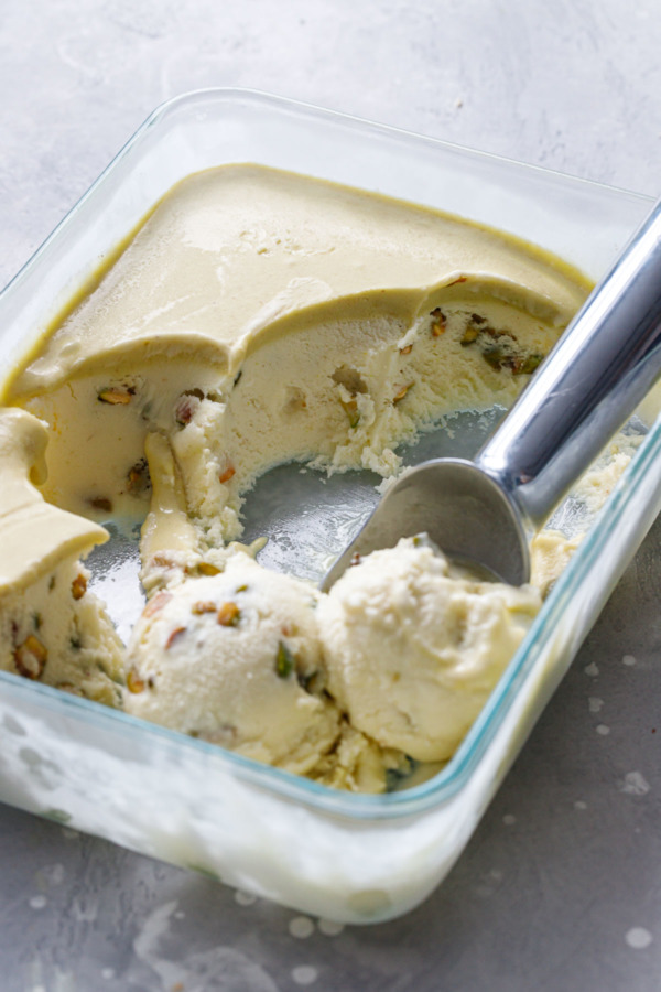 Pistachio gelato in a shallow dish with a layer of pistachio cream on top, with an ice cream scoop and melting scoops of gelato.