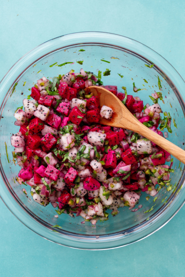 Glass bowl filled with pink and white dragonfruit salsa on a turquoise background