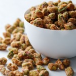 A white porcelain bowl overflowing with spiced candied pistachios on a marble surface