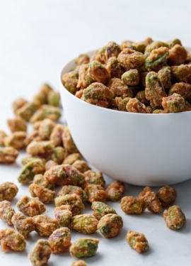 A white porcelain bowl overflowing with spiced candied pistachios on a marble surface