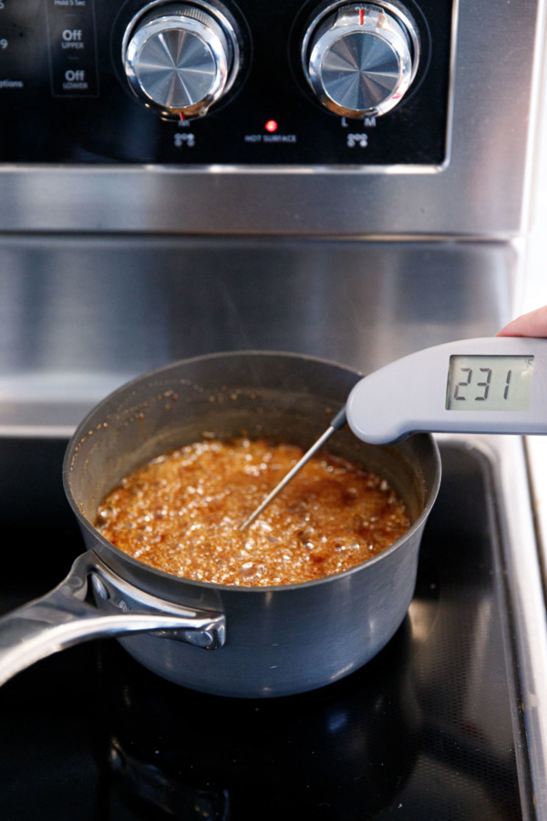A thermometer inserted into a small saucepan with boiling sugar and spices