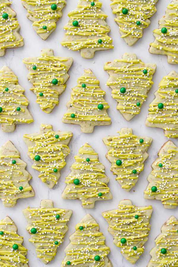 Alternating rows of pistachio Christmas tree cookies on a marble background