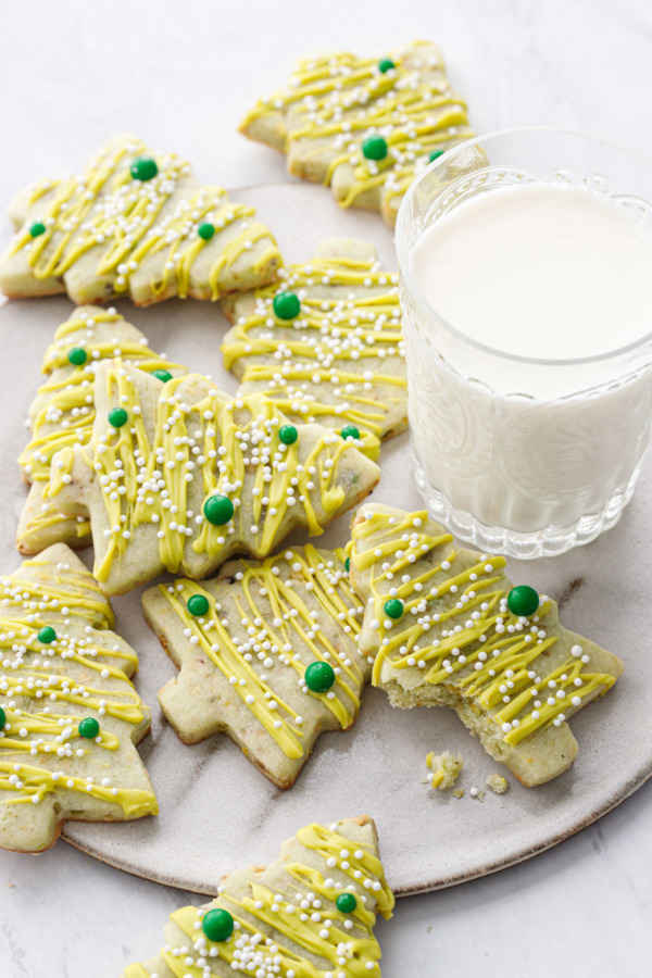 A pile of tree-shaped Pistachio sugar cookies on a plate with a glass of milk.
