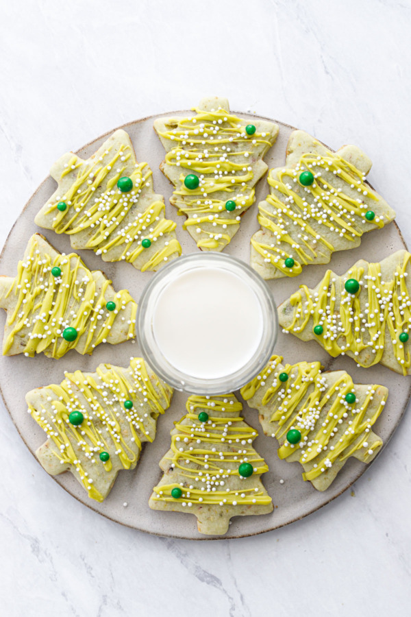 Top down view of tree shaped pistachio sugar cookies arranged in a burst shape around a glass of milk