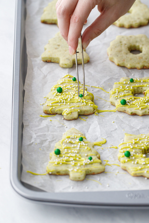 Using a pair of tweezers to place the green ball sprinkles onto the cookies.