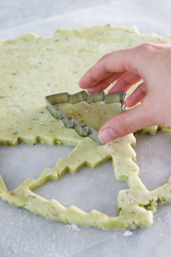 Cutting out tree-shapes out of a rolled out piece of pistachio sugar cookie dough