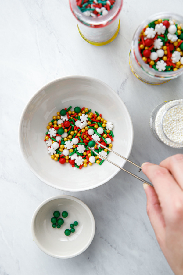 A pair of tweezers picking out the green ball sprinkles from holiday sprinkle blends.