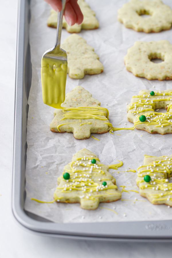 Using a fork to drizzle the melted green candy coating on tree-shaped cookies.