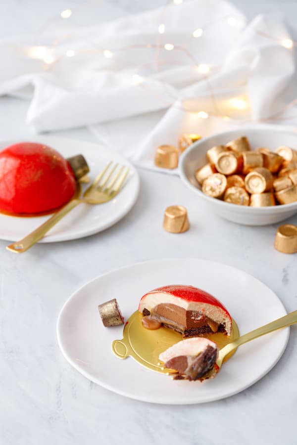 Christmas Ornament Cakes on a white background with fairy lights, one cake cut in half to show the cross-section of layers.