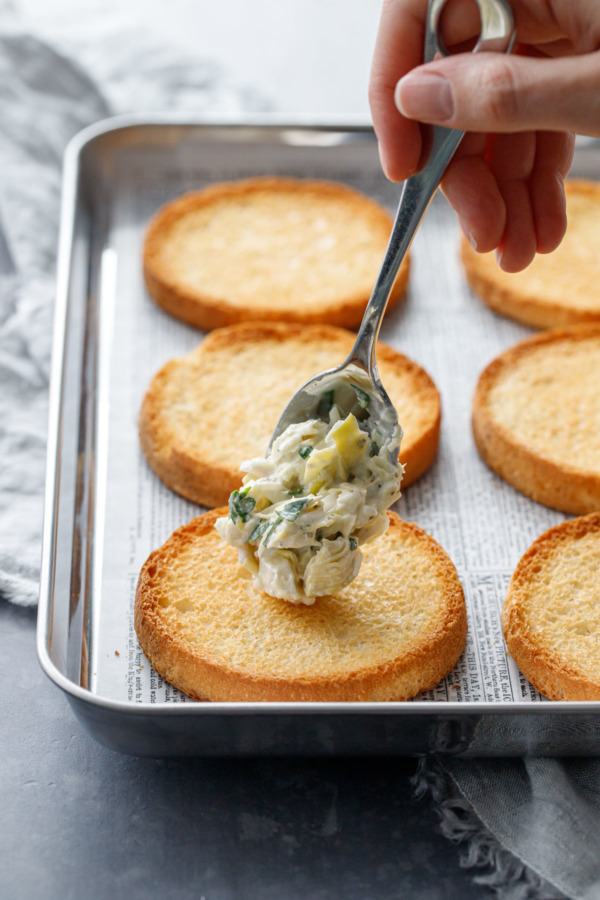 Spooning the cheesy artichoke topping onto the crostino toasts