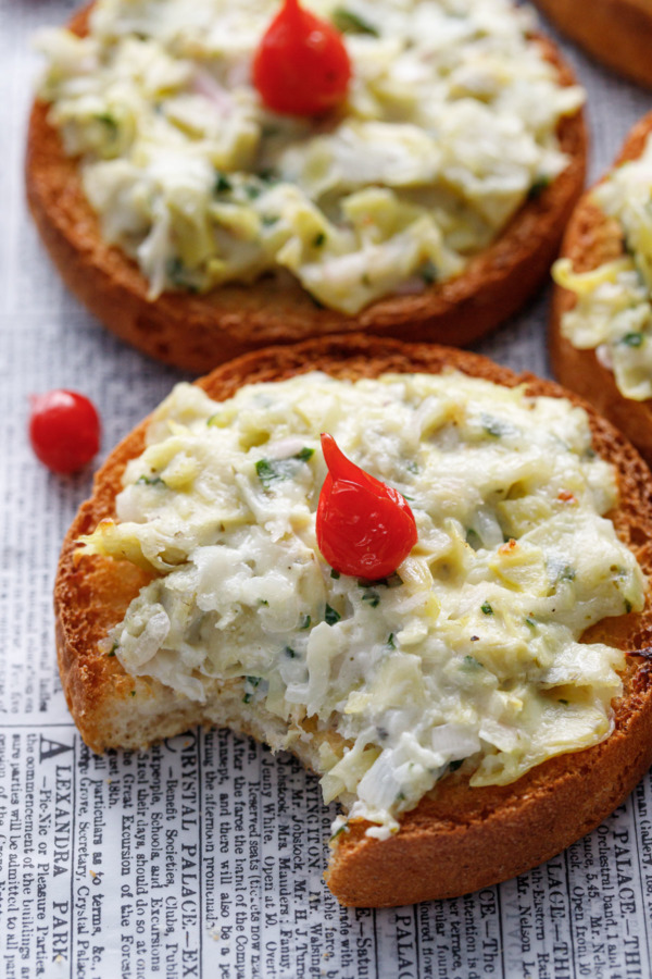 Closeup of one artichoke crostino toast with a pepper drop on top with a bite taken out of it.