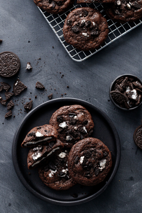 Overhead shot of Cream-Stuffed Chocolate Cookies 'n Cream Cookies on a black plate with crushed cookies scattered around.