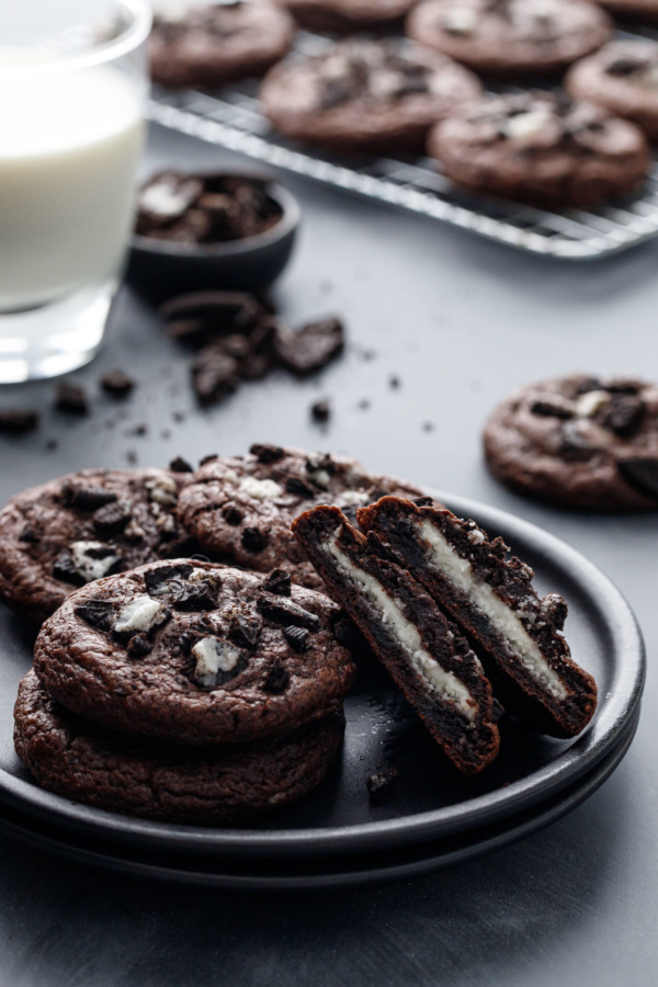 Cream-Stuffed Chocolate Cookies 'n Cream Cookies on a plate, one cut in half to show the cream stuffing, with a glass of milk and crumbled cookies in the background.