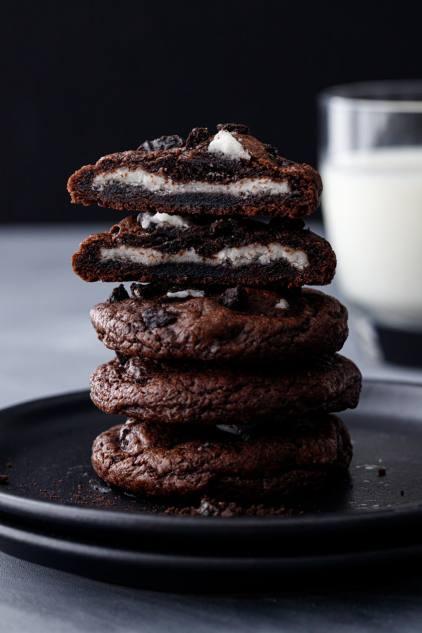 Stack of 4 Cream-Stuffed Chocolate Cookies 'n Cream Cookies, one cut in half to show the cream filling, with a glass of milk in the background.