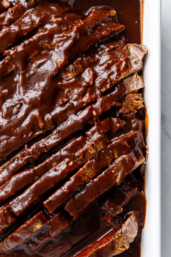 Sliced beef brisket arranged in a baking dish, smothered in a thick sauce