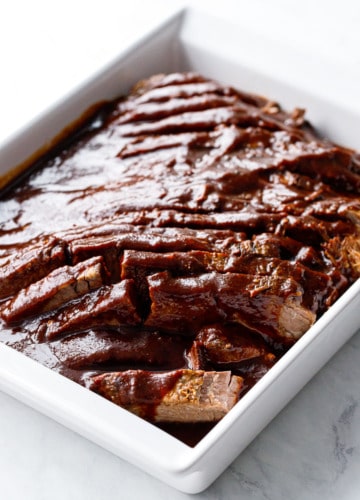 Modern white baking dish with sliced beef brisket and sauce poured over top