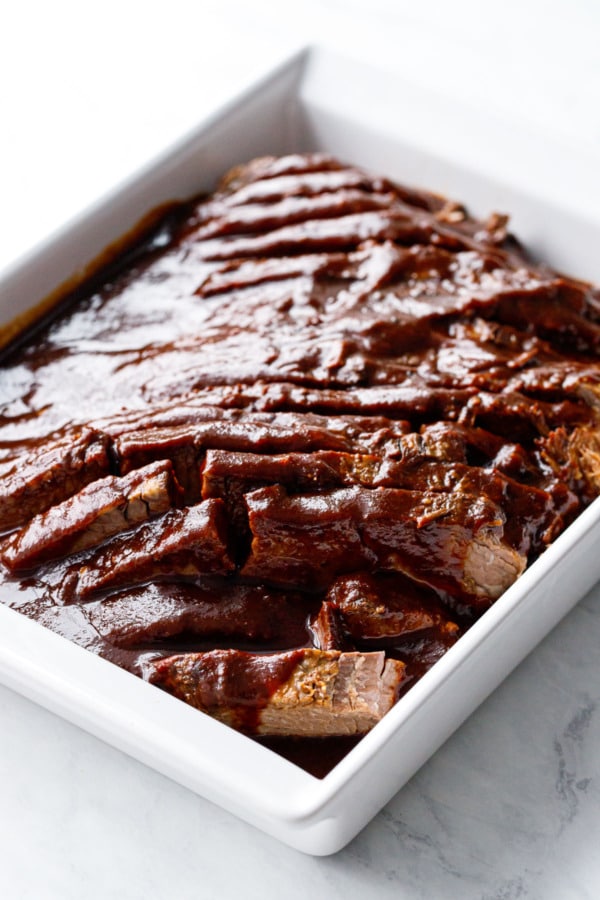 Modern white baking dish with sliced beef brisket and sauce poured over top