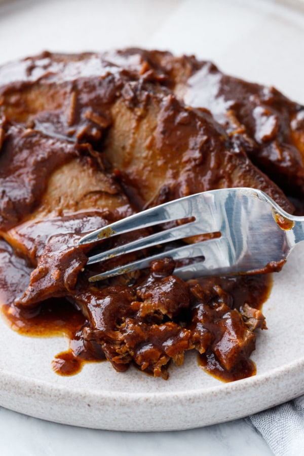 Extreme closeup of a fork flaking off pieces of ultra tender slow cooker beef brisket