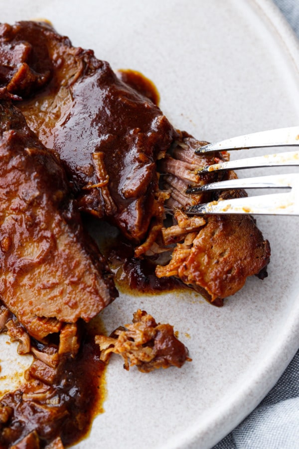 Extreme closeup of a fork flaking off pieces of ultra tender slow cooker beef brisket