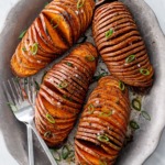 Overhead view of four Hasselback Sweet Potatoes arranged on a metal plate with forks