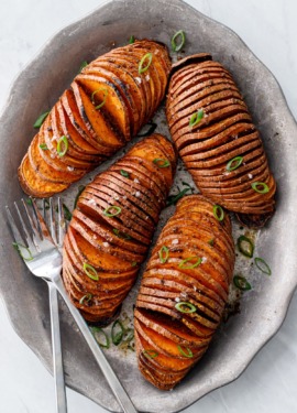 Overhead view of four Hasselback Sweet Potatoes arranged on a metal plate with forks