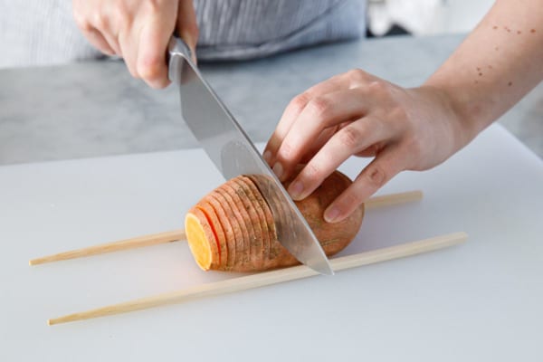 Using chopsticks as guides to slice the sweet potato into very thin slices.