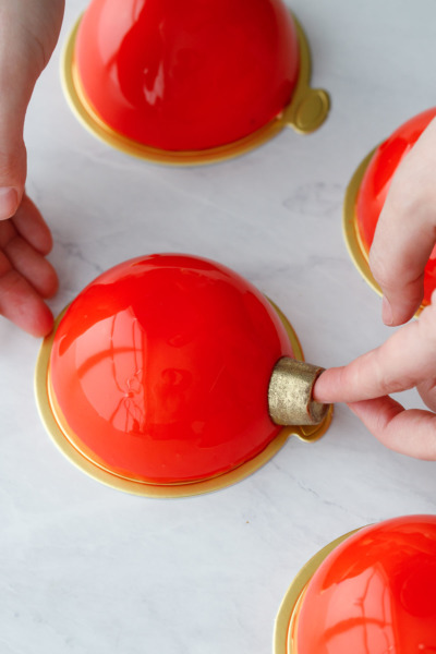 How-To Entremet Cake Process: place a gold-dusted Rolo candy on one side of the cake.